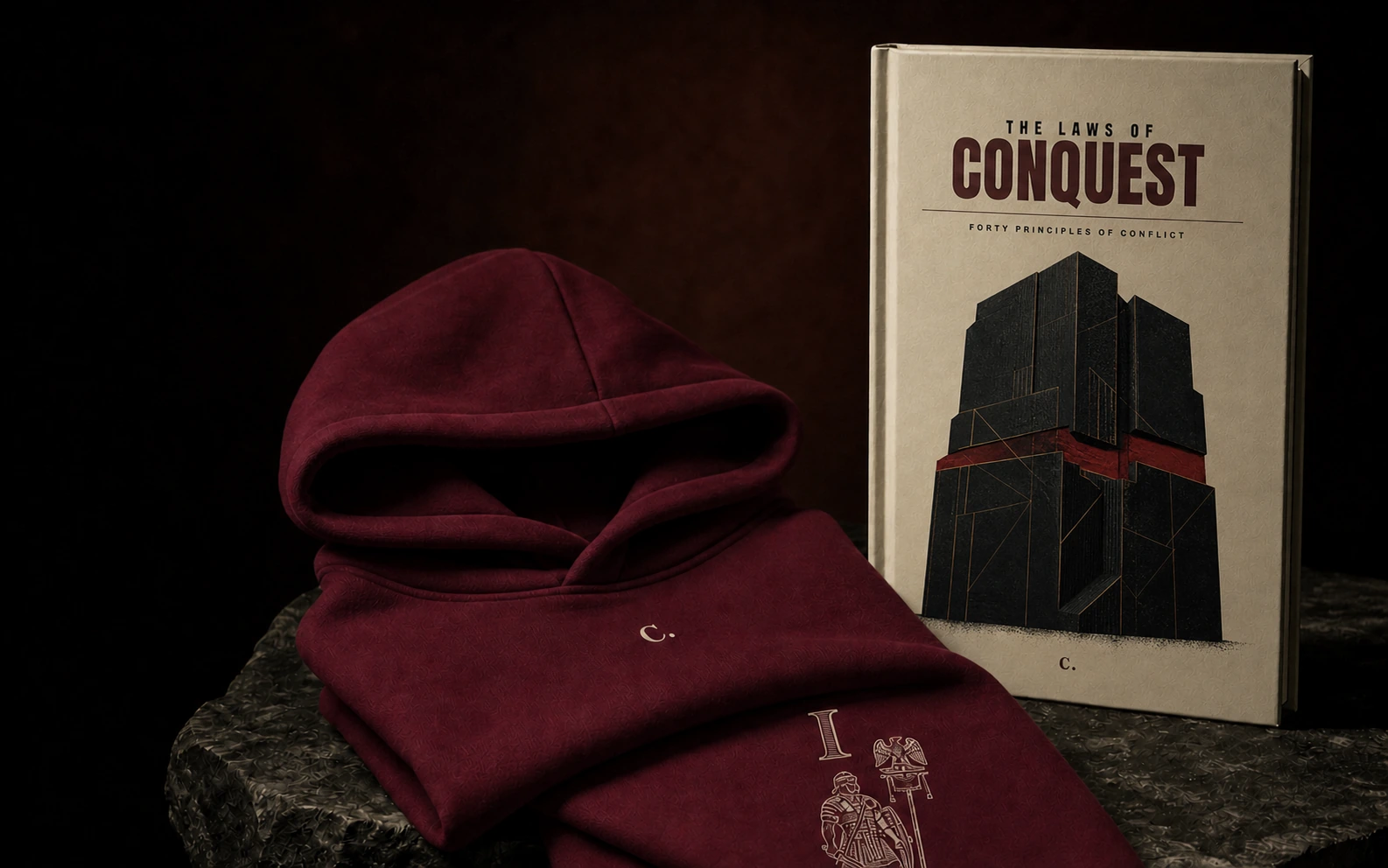 The Laws of Conquest building-cover hardback beside the oxblood Law Hoodie